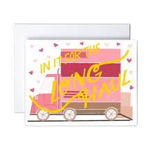 Load image into Gallery viewer, pink, dark pink, and shades of brown moving van with boxes ready to load and pink hearts with yellow &#39;in it for the long haul&#39; script text over the front greeting card
