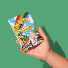 Load image into Gallery viewer, hand holding pride parade during a bright and sunny day with yellow balloons spelling out &#39;happy pride&#39; over numerous pride flags and a rainbow in the background greeting card
