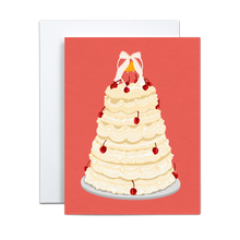 Load image into Gallery viewer, off white wedding cake with several tiers and cherries on a silver platter and a small wedding bell figurine on top with a bow on a salmon pink background greeting card
