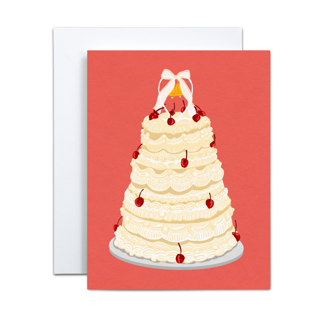 off white wedding cake with several tiers and cherries on a silver platter and a small wedding bell figurine on top with a bow on a salmon pink background greeting card